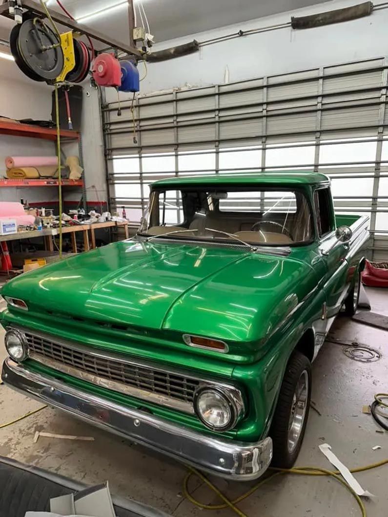 A green truck is parked in a garage next to a garage door.