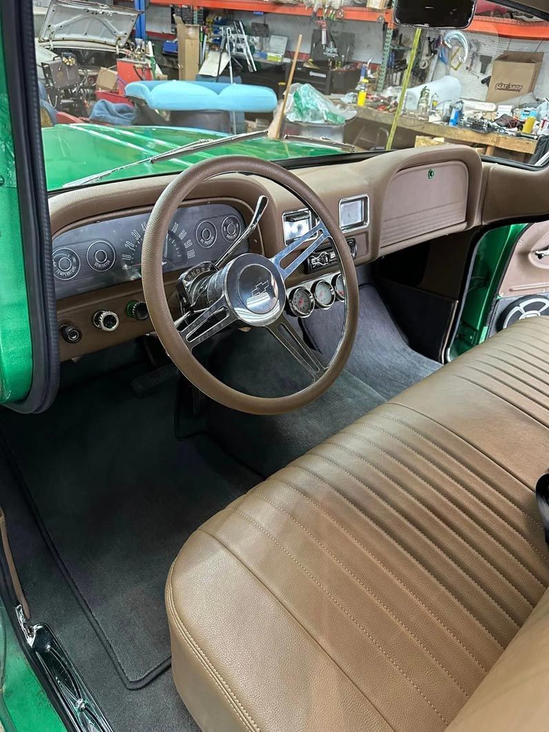 The interior of a green truck with a brown seat and steering wheel.
