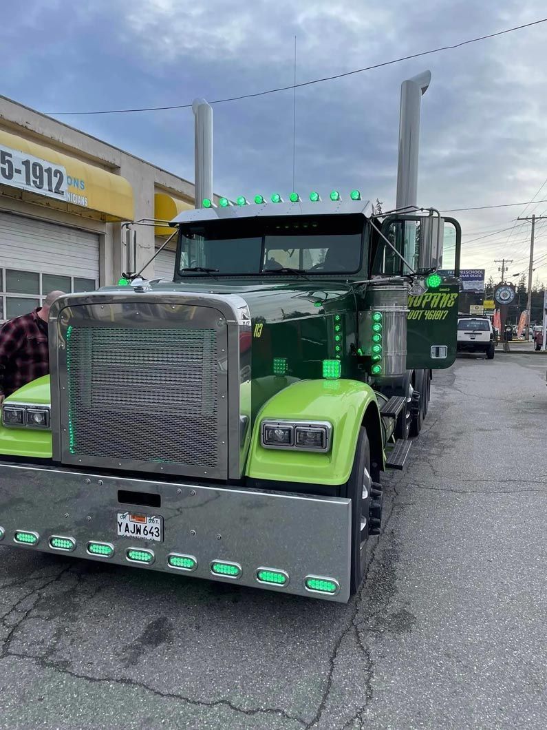 A green semi truck is parked on the side of the road in front of a building.