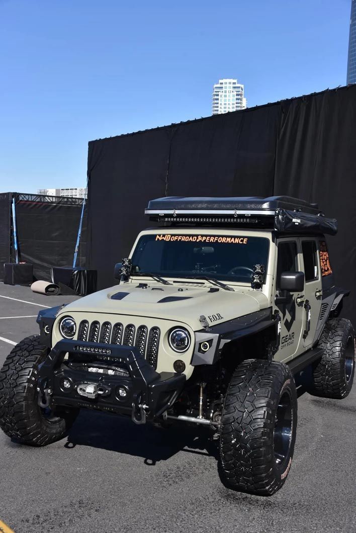 A jeep with a tent on top of it is parked in front of a building.