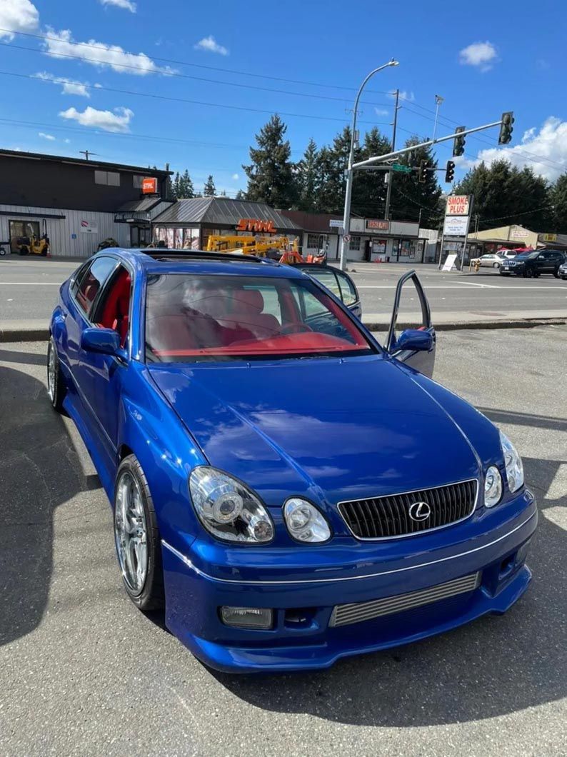 A blue car is parked on the side of the road in a parking lot.