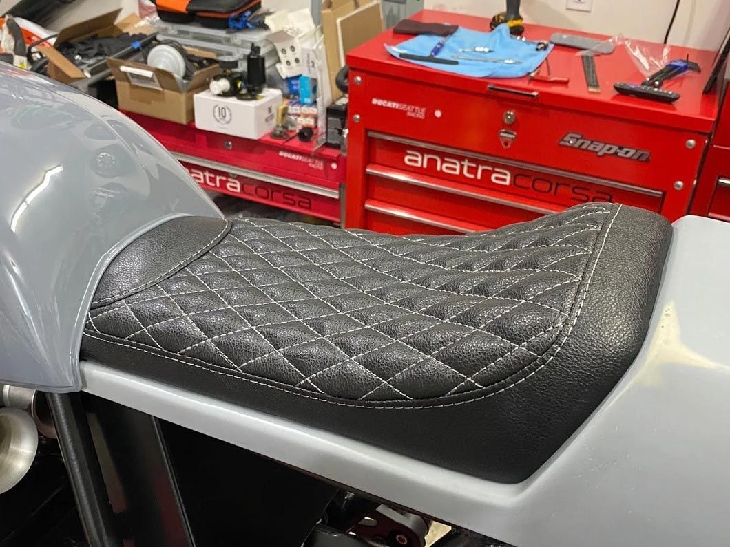 A motorcycle seat is sitting in front of a red snap on toolbox.
