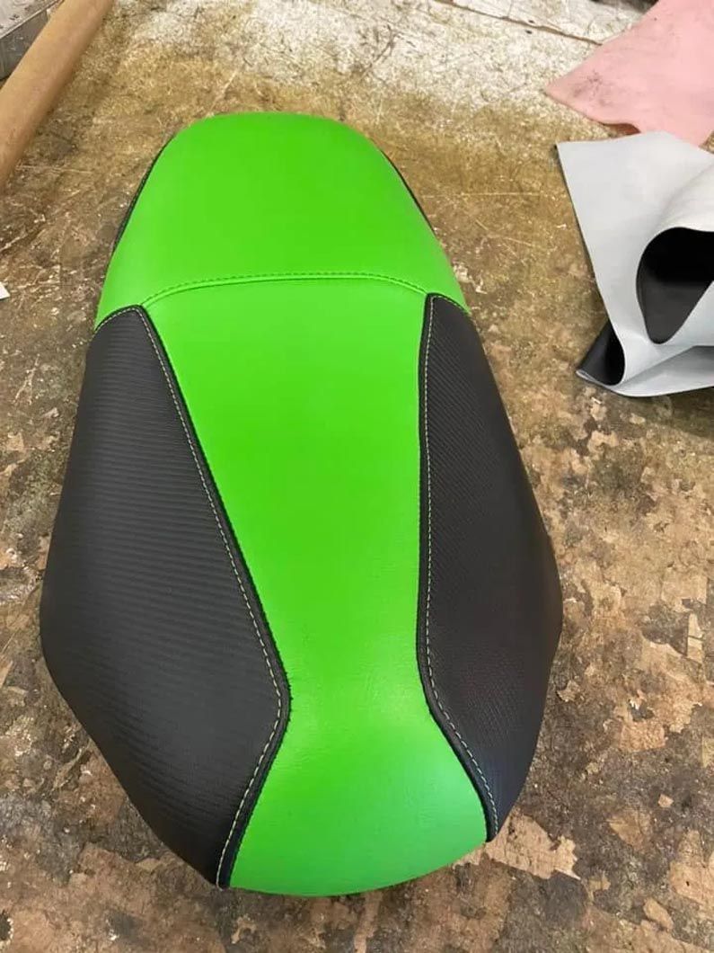 A green and black motorcycle seat is sitting on a wooden table.