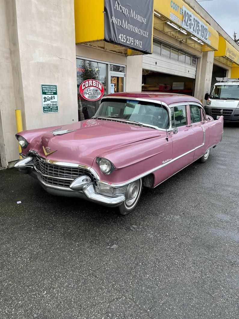 A pink cadillac is parked in front of a car dealership.