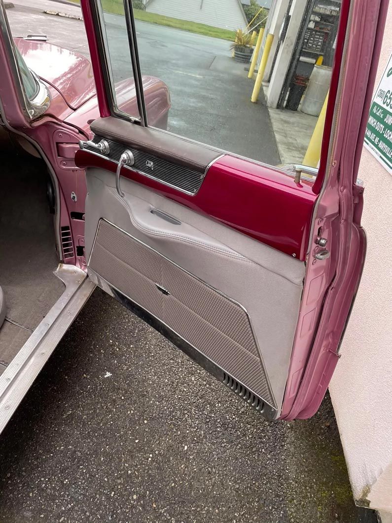 A pink car with the door open is parked on the side of the road.