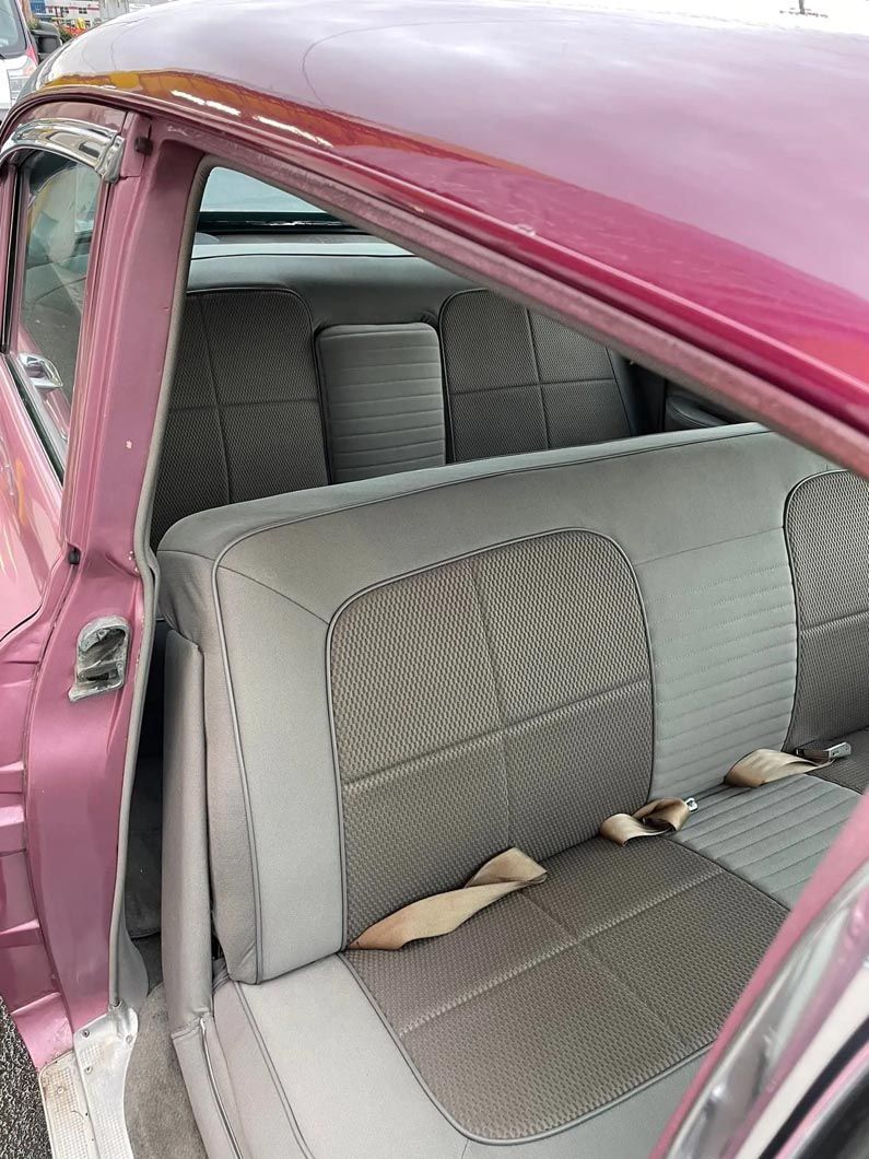 The back seat of a pink car with the door open.