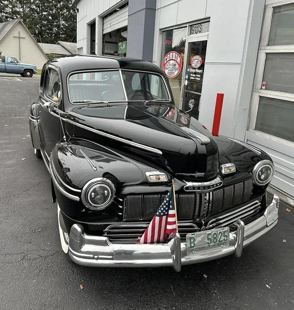A black car with an american flag on the front is parked in front of a garage.