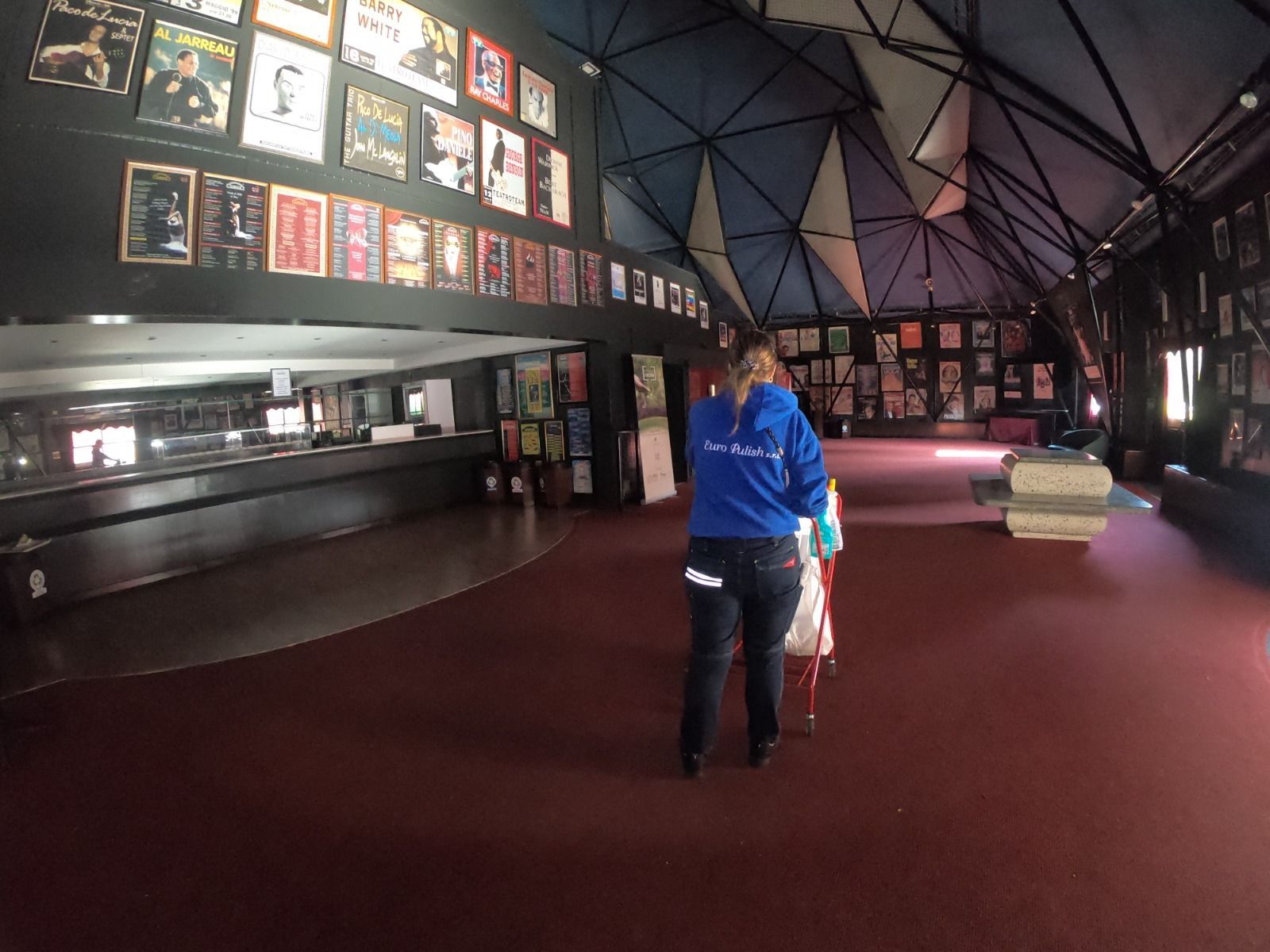 Una persona con una felpa blu accompagna un bambino attraverso una stanza con dei poster alle pareti.