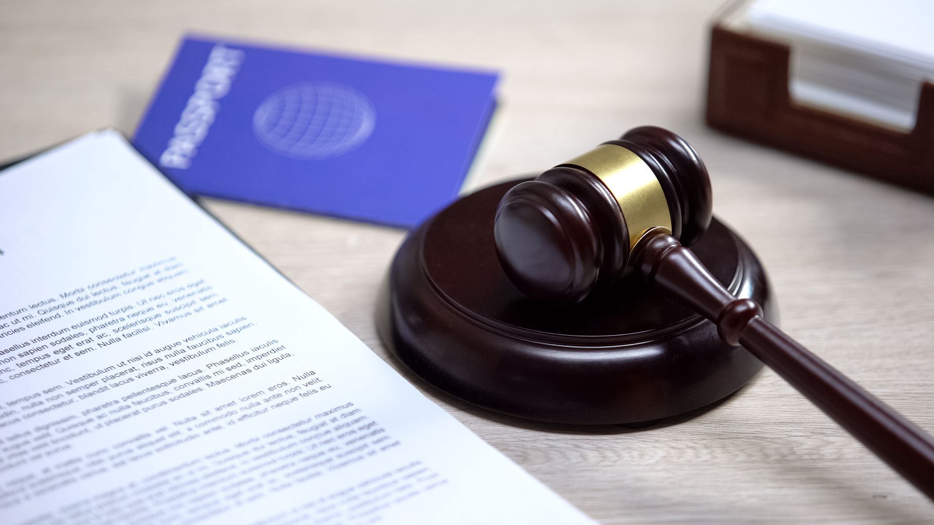 A judge 's gavel is sitting on a wooden table next to a passport and a piece of paper.