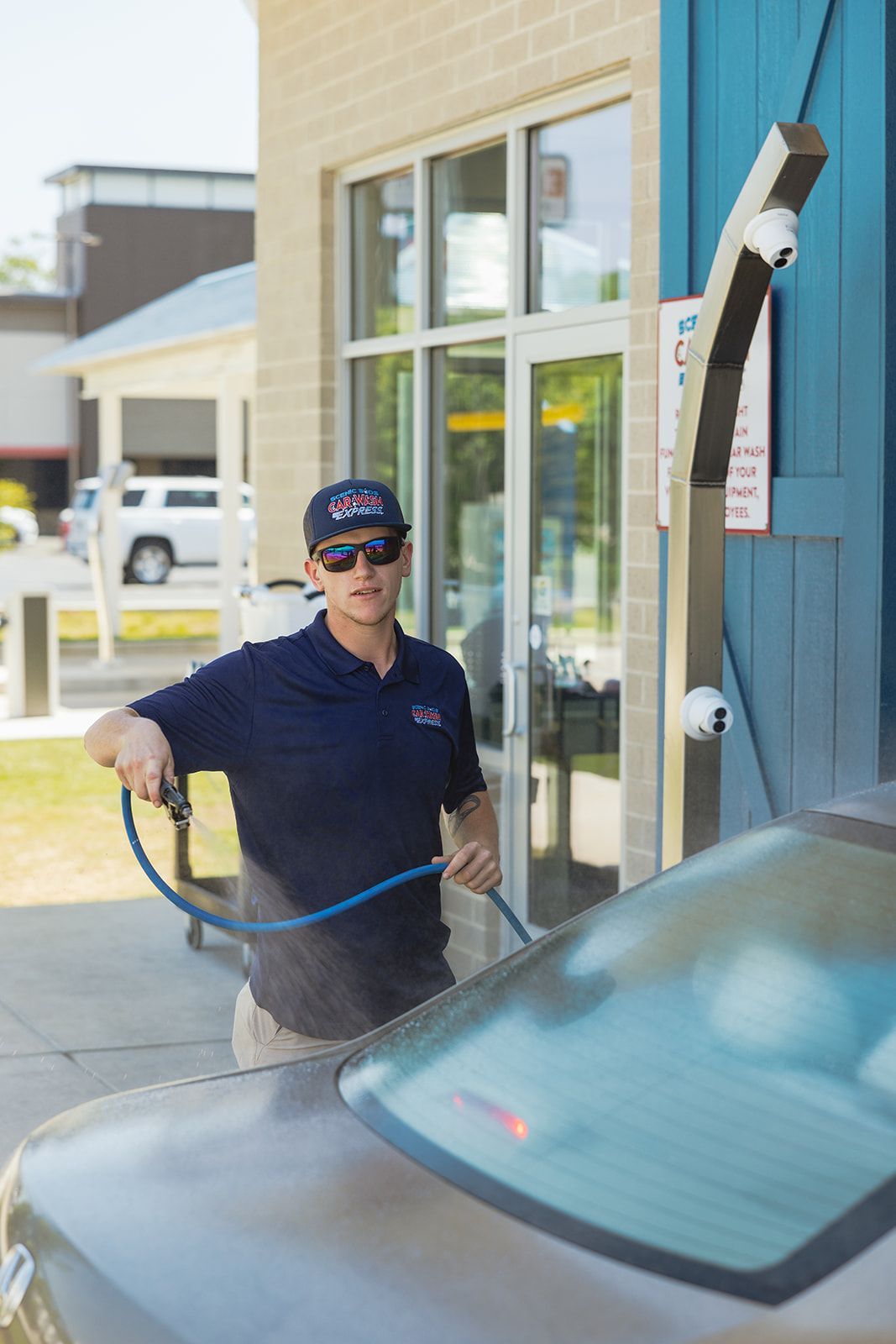 A man is washing a car with a hose at a car wash.