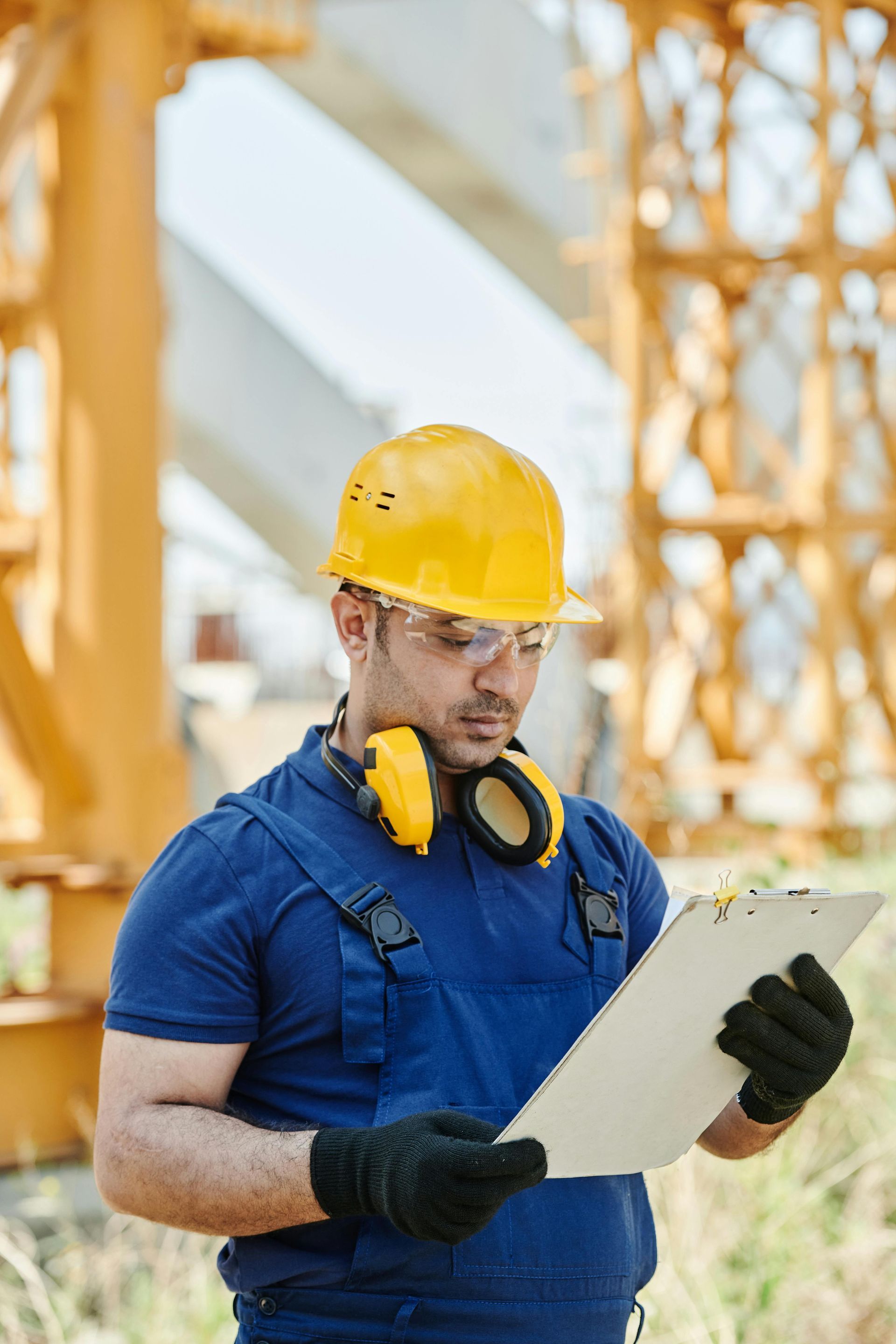 A construction worker wearing a hard hat and headphones is looking at a clipboard.