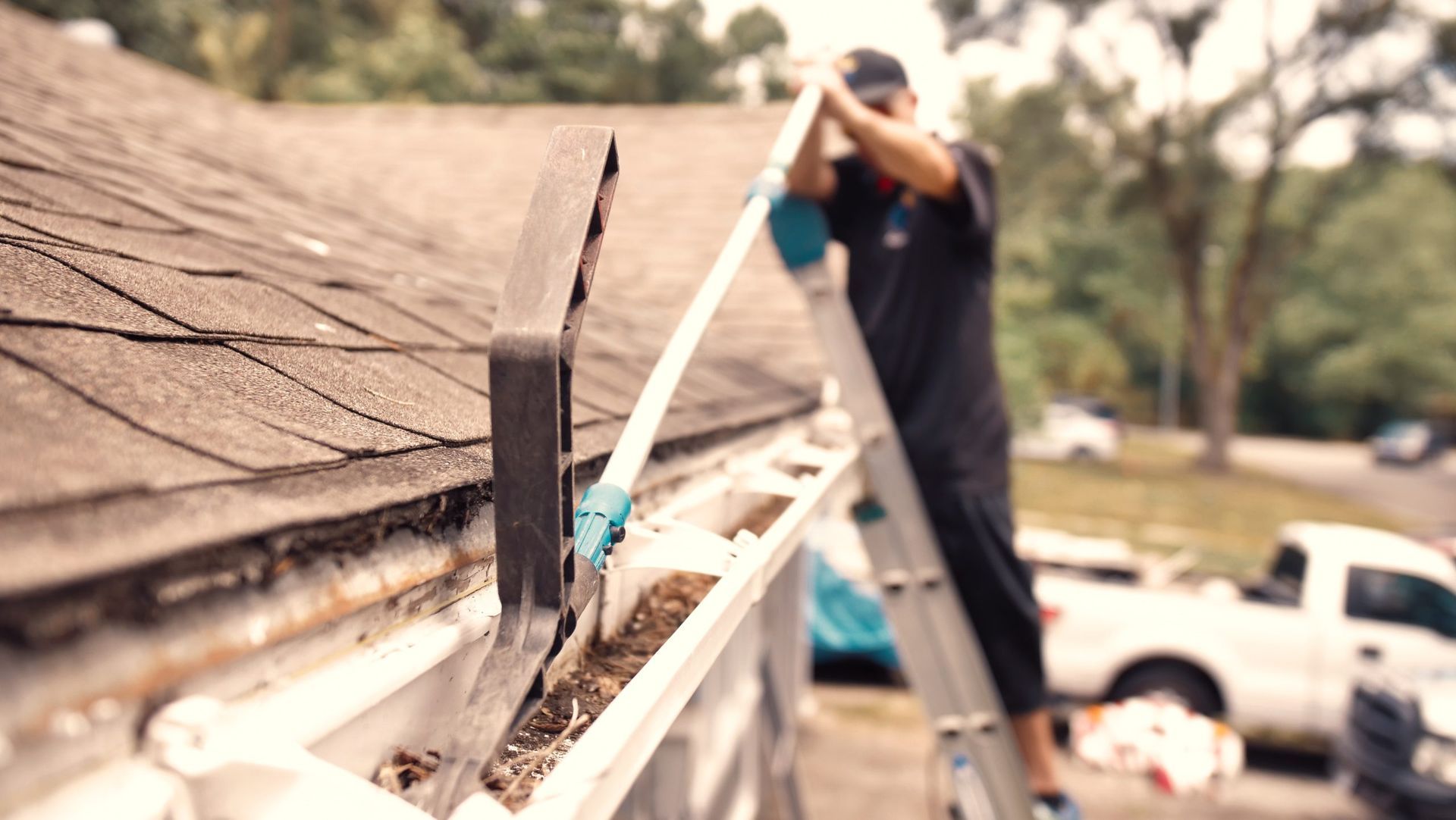 A man on a ladder is cleaning a gutter on a roof.