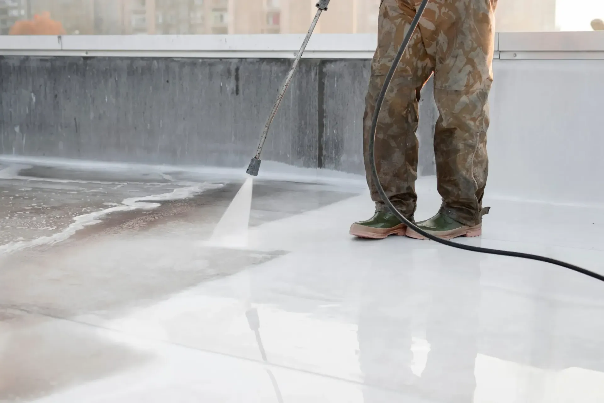 A man is using a high pressure washer to clean a roof.