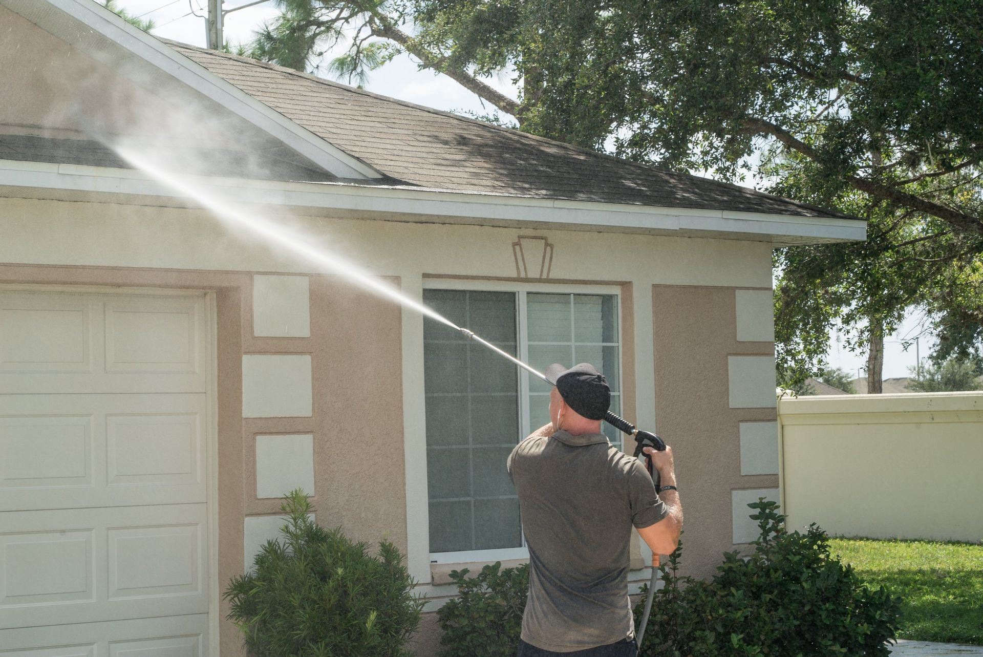 A man is using a high pressure washer to clean the roof of a house.