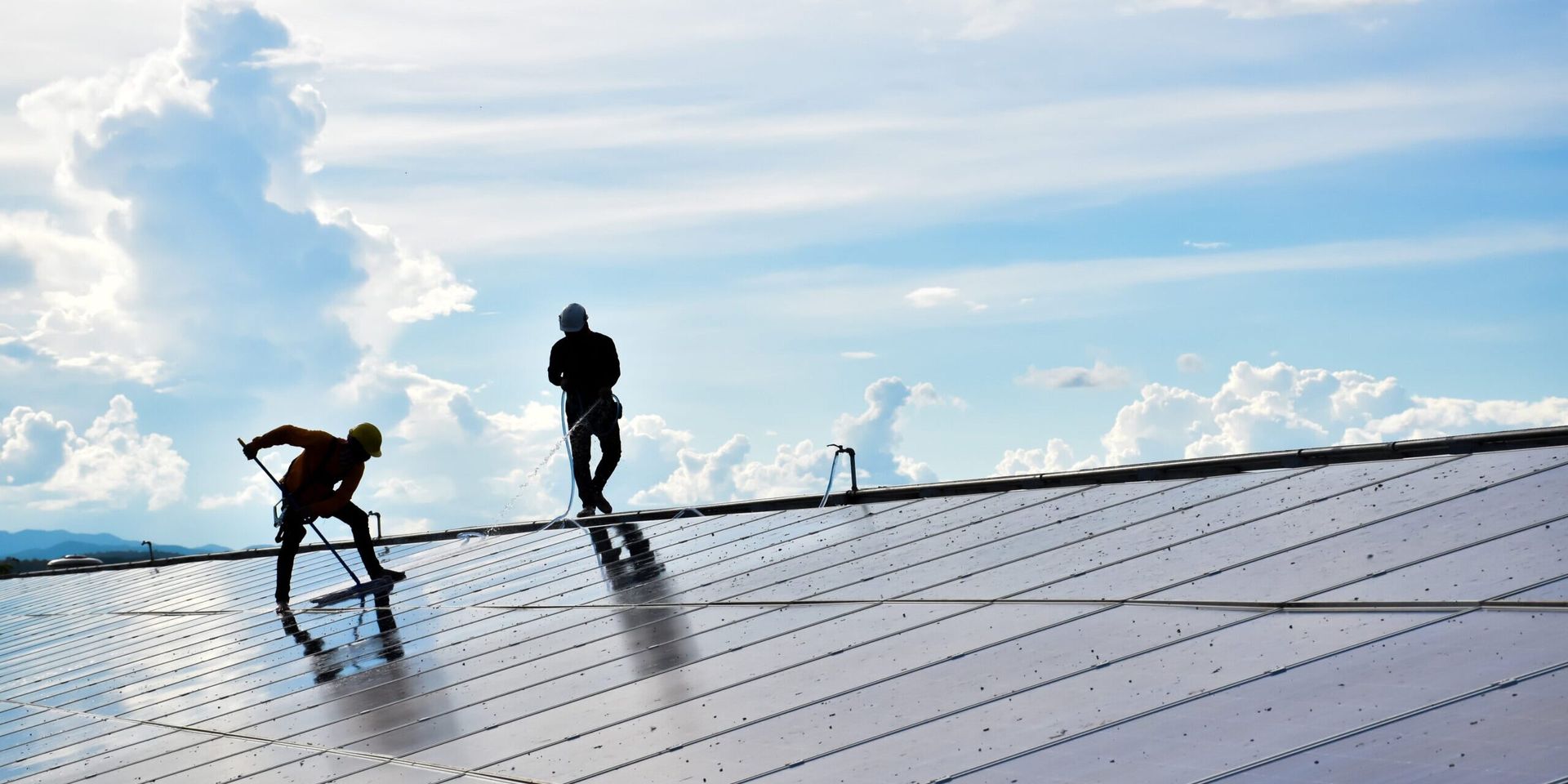 Two men are working on a roof with solar panels.