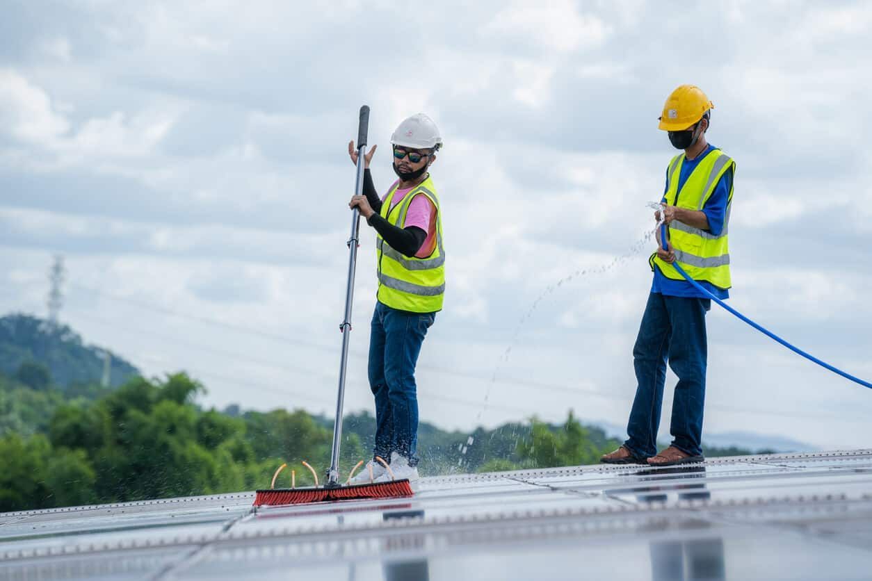 Two construction workers are cleaning the roof of a building.