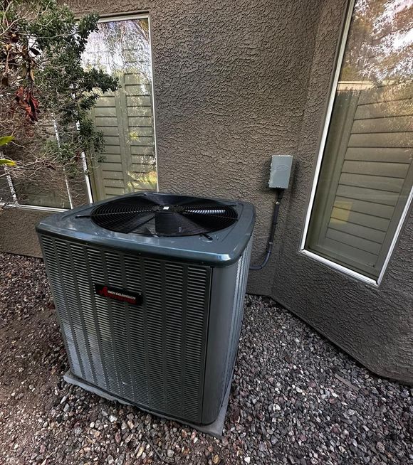 A large air conditioner is sitting outside of a building next to a window.