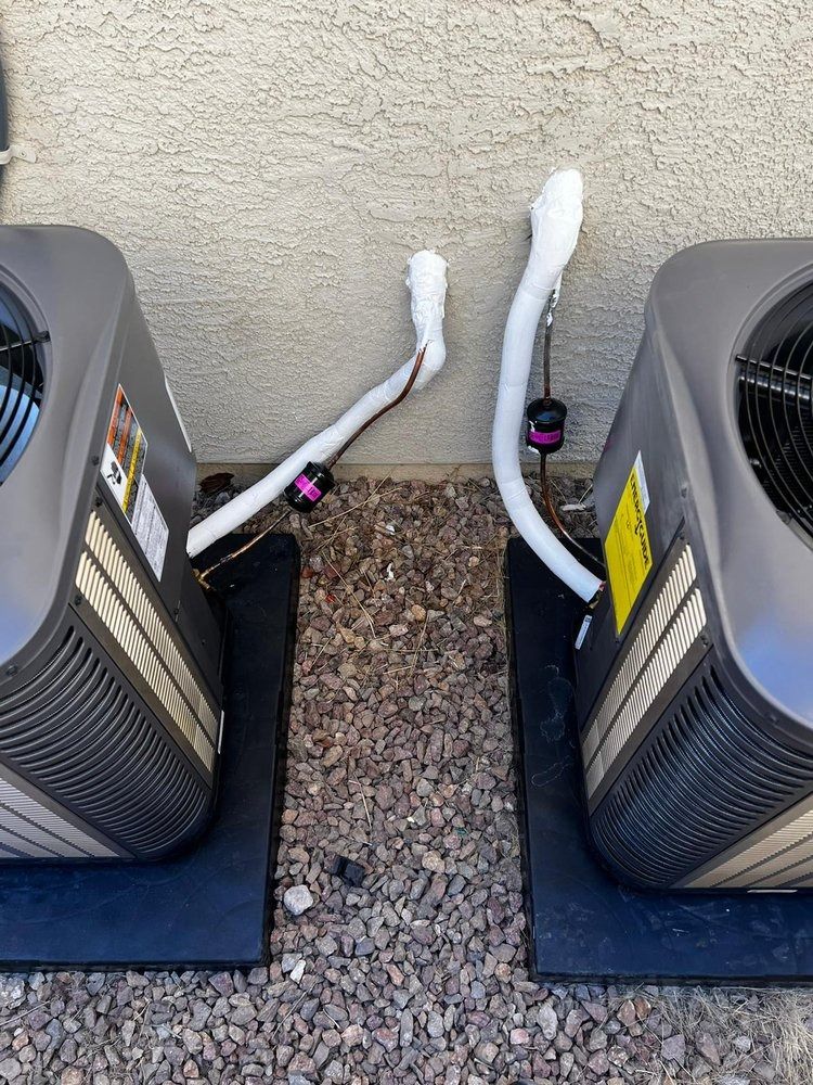 Two air conditioners are sitting next to each other on a gravel floor.