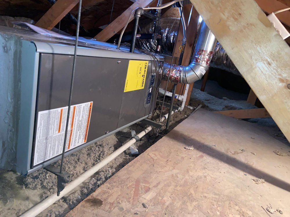 An air conditioner is hanging from the ceiling of an attic.