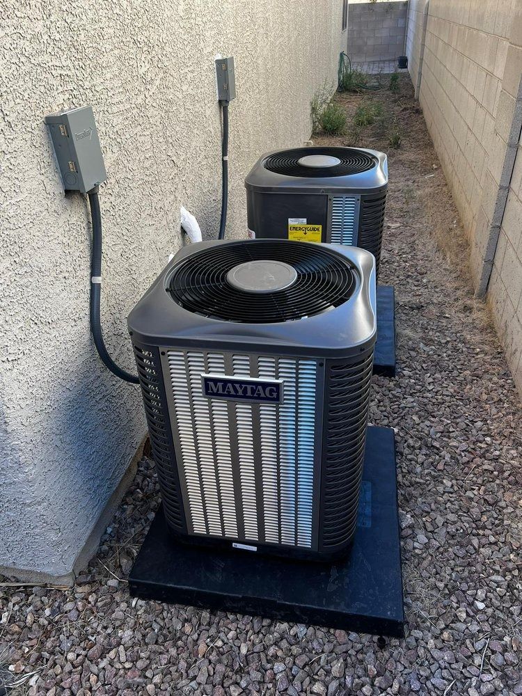 Two air conditioners are sitting next to each other on gravel in a backyard.