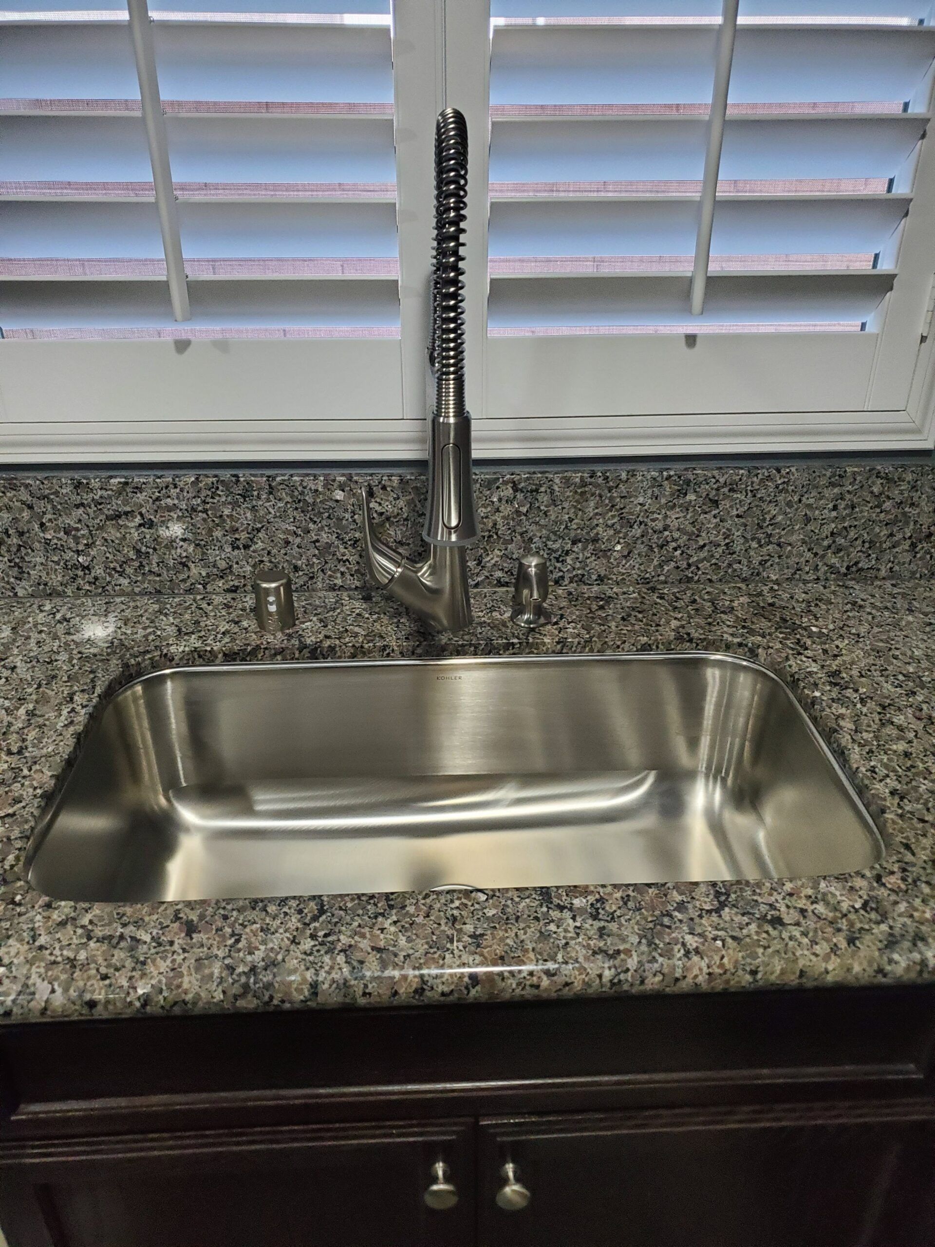 A stainless steel kitchen sink with a faucet on a granite counter top.