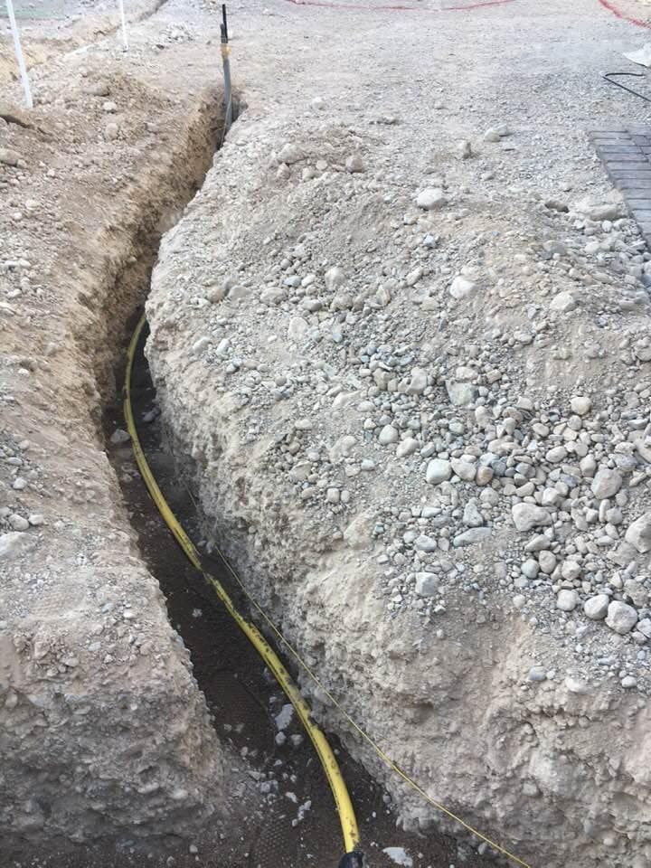 A yellow hose is laying in the dirt in a trench.