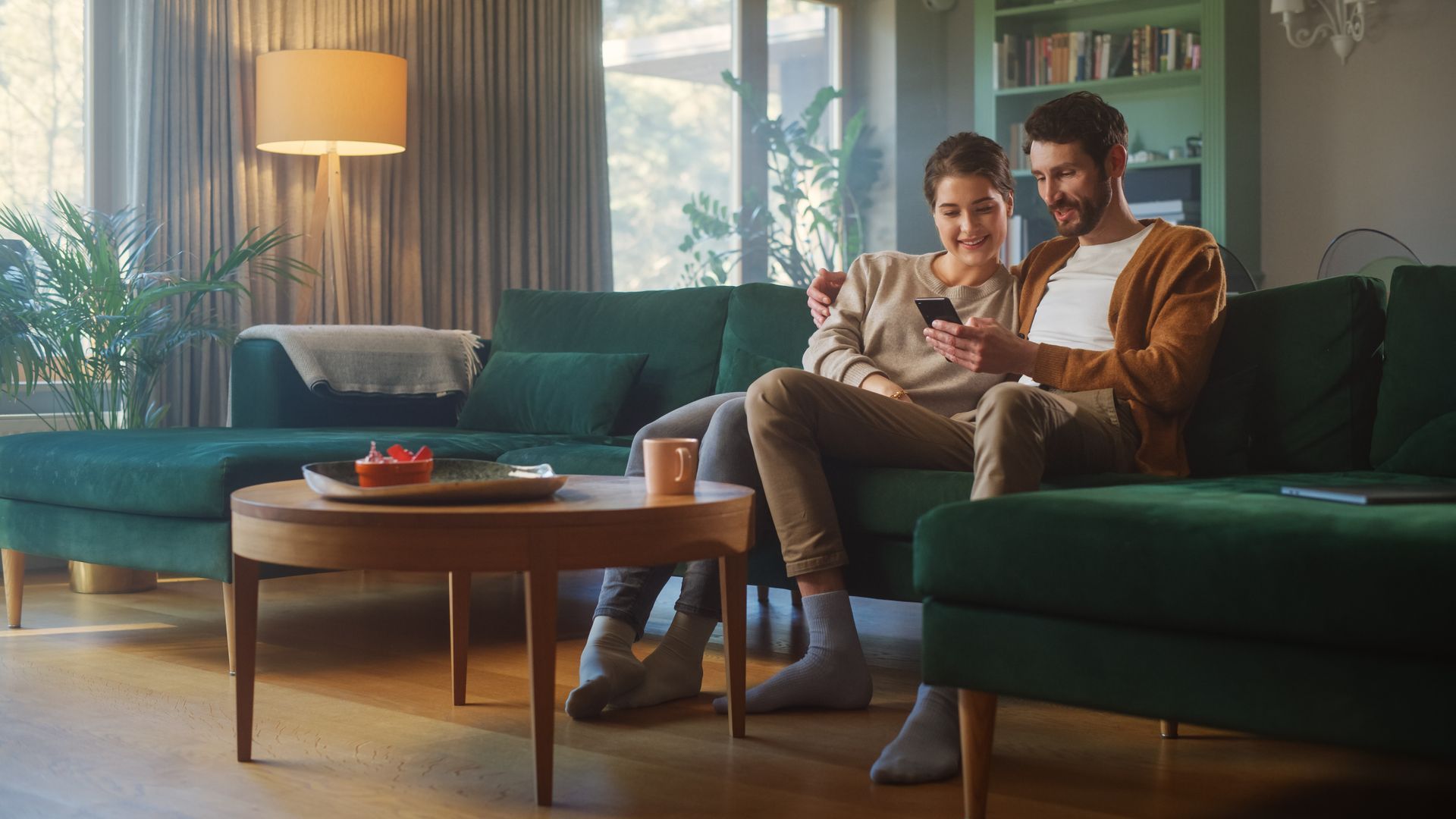A man and a woman are sitting on a couch looking at a cell phone.