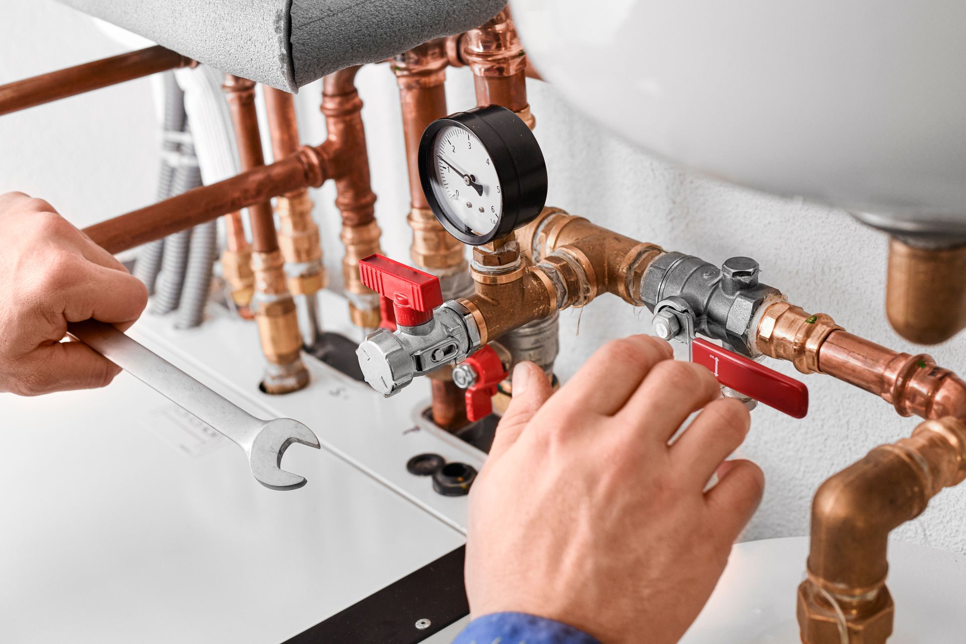 A plumber is working on a water heater with a wrench.