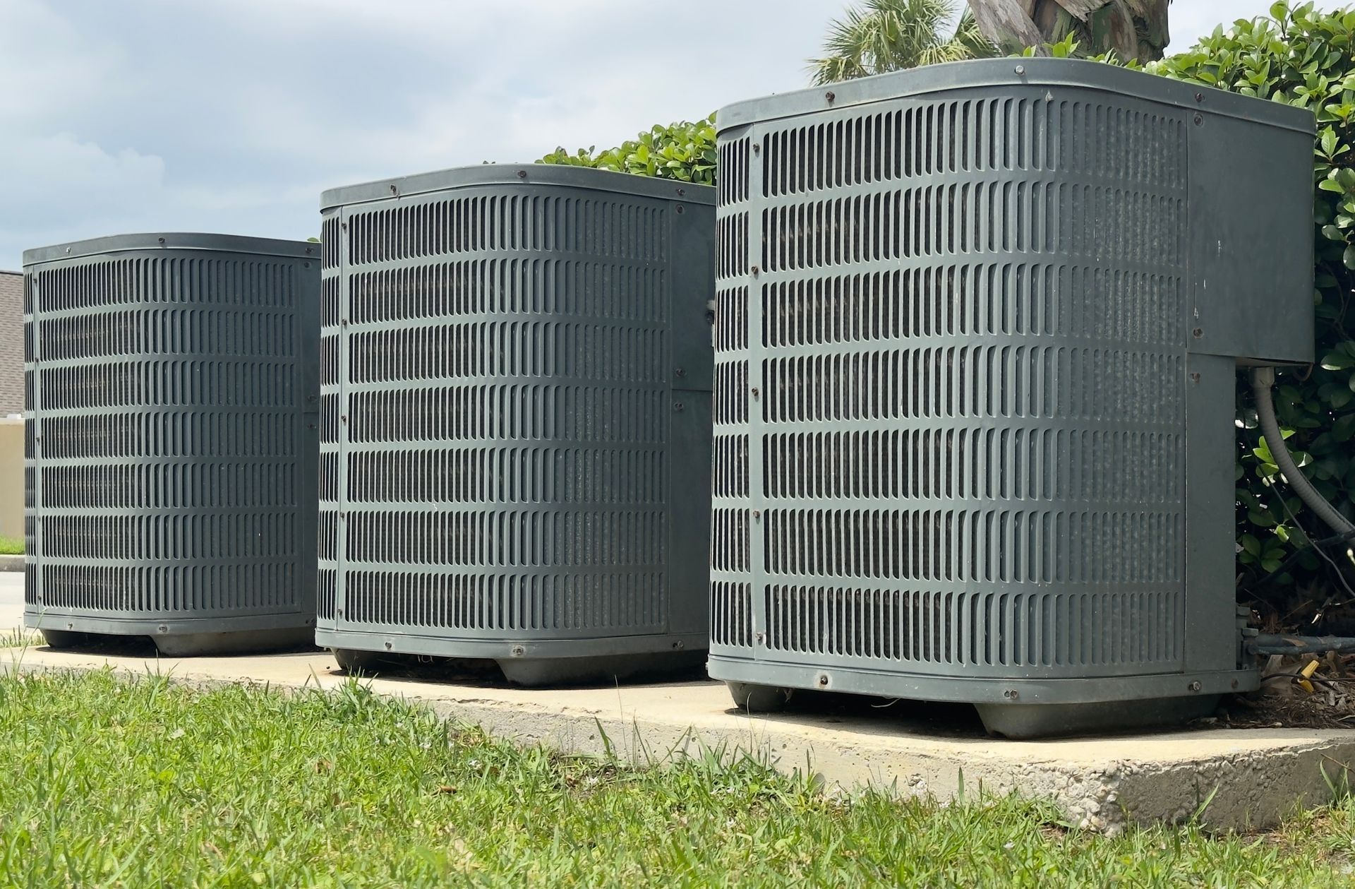Three air conditioners are sitting next to each other on a sidewalk.