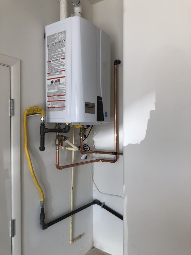 A white water heater is hanging on a wall next to copper pipes.