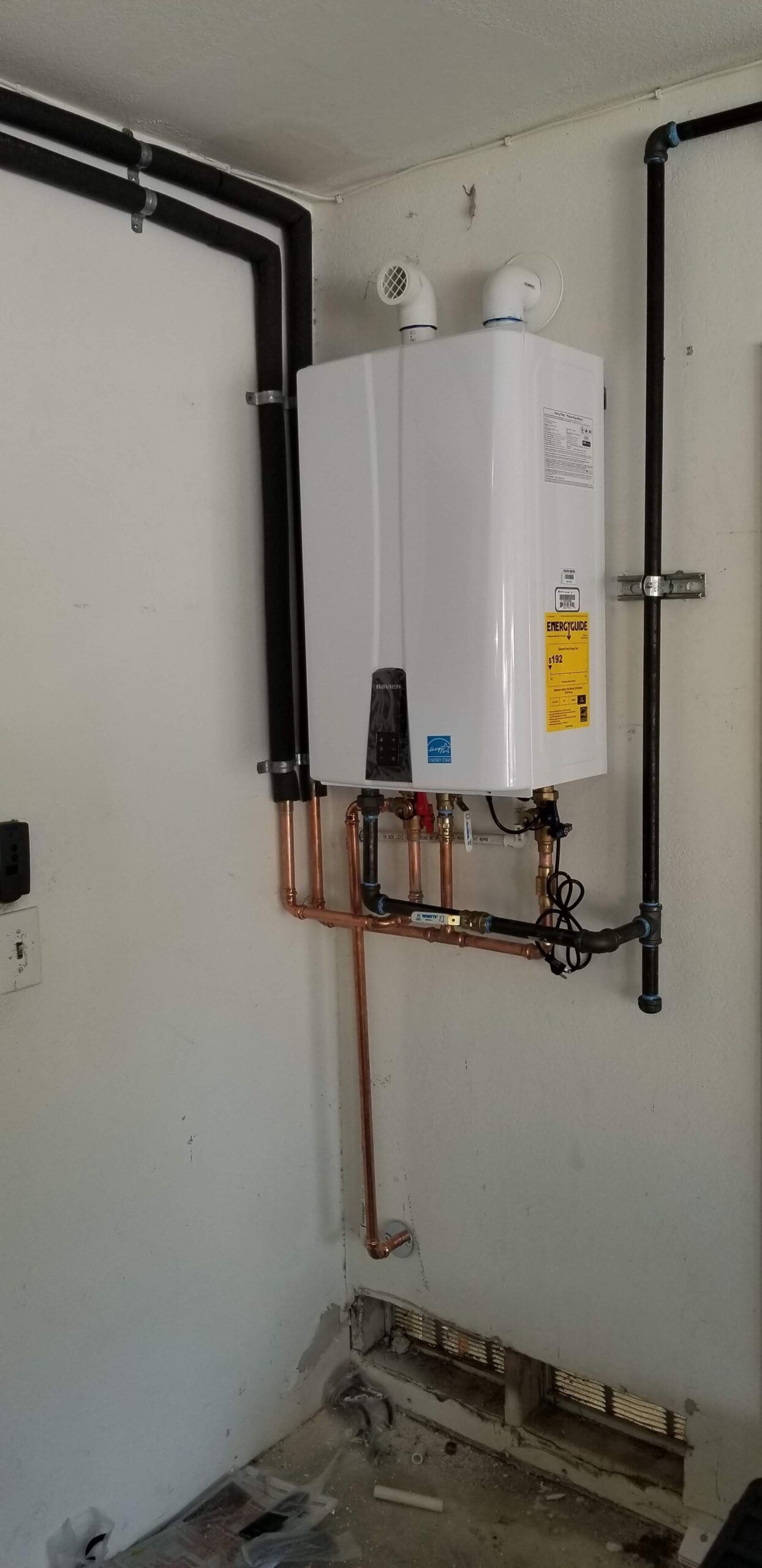 A white water heater is hanging on a wall in a room.