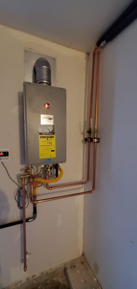 A water heater is hanging on a wall next to copper pipes.