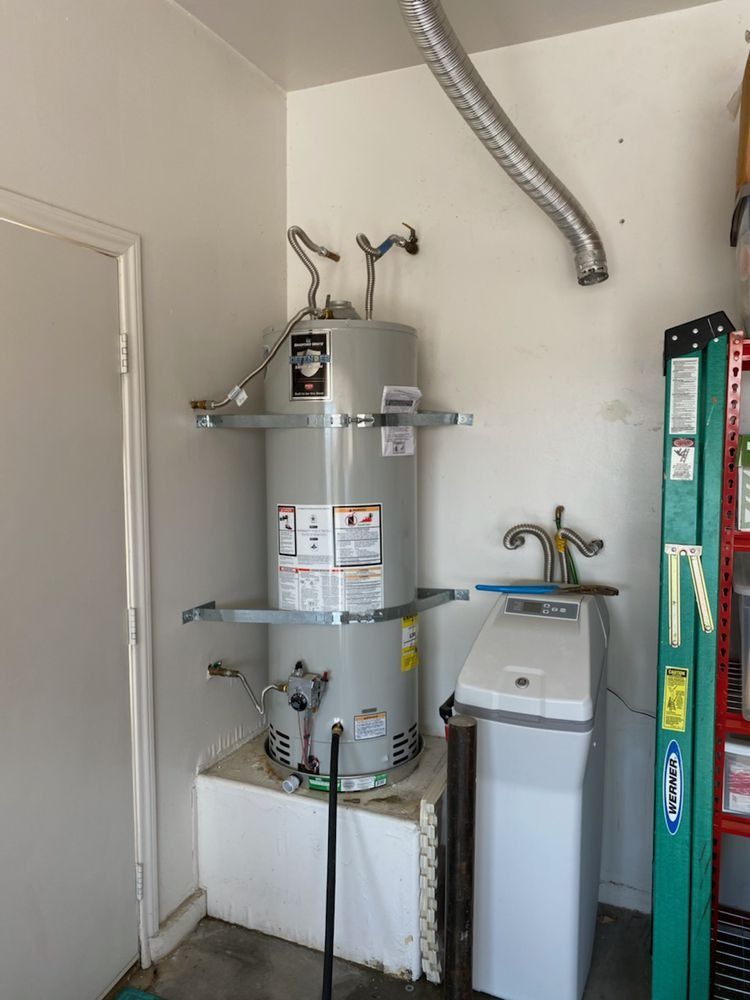 A water heater is sitting next to a washer and dryer in a garage.