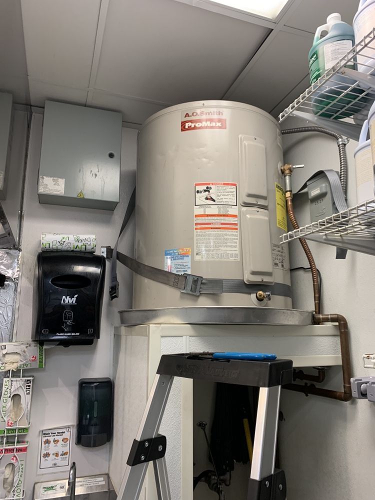 A water heater is sitting in a room next to a ladder.