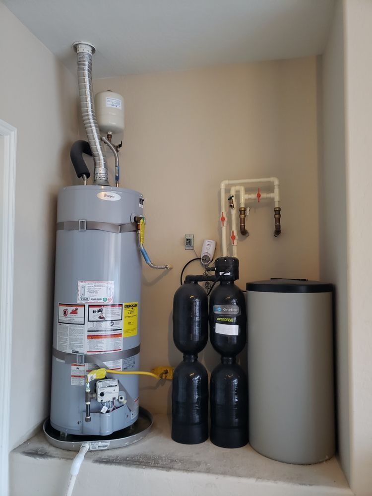 A water heater is sitting in a corner of a room next to a tank.