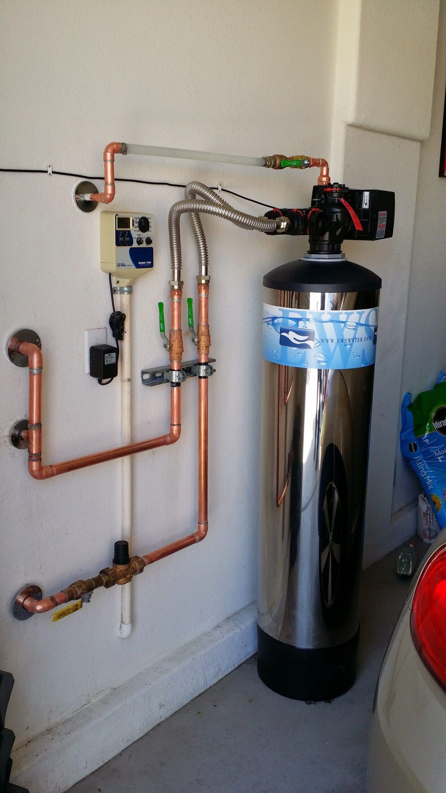 A stainless steel water filter is attached to a wall in a garage.