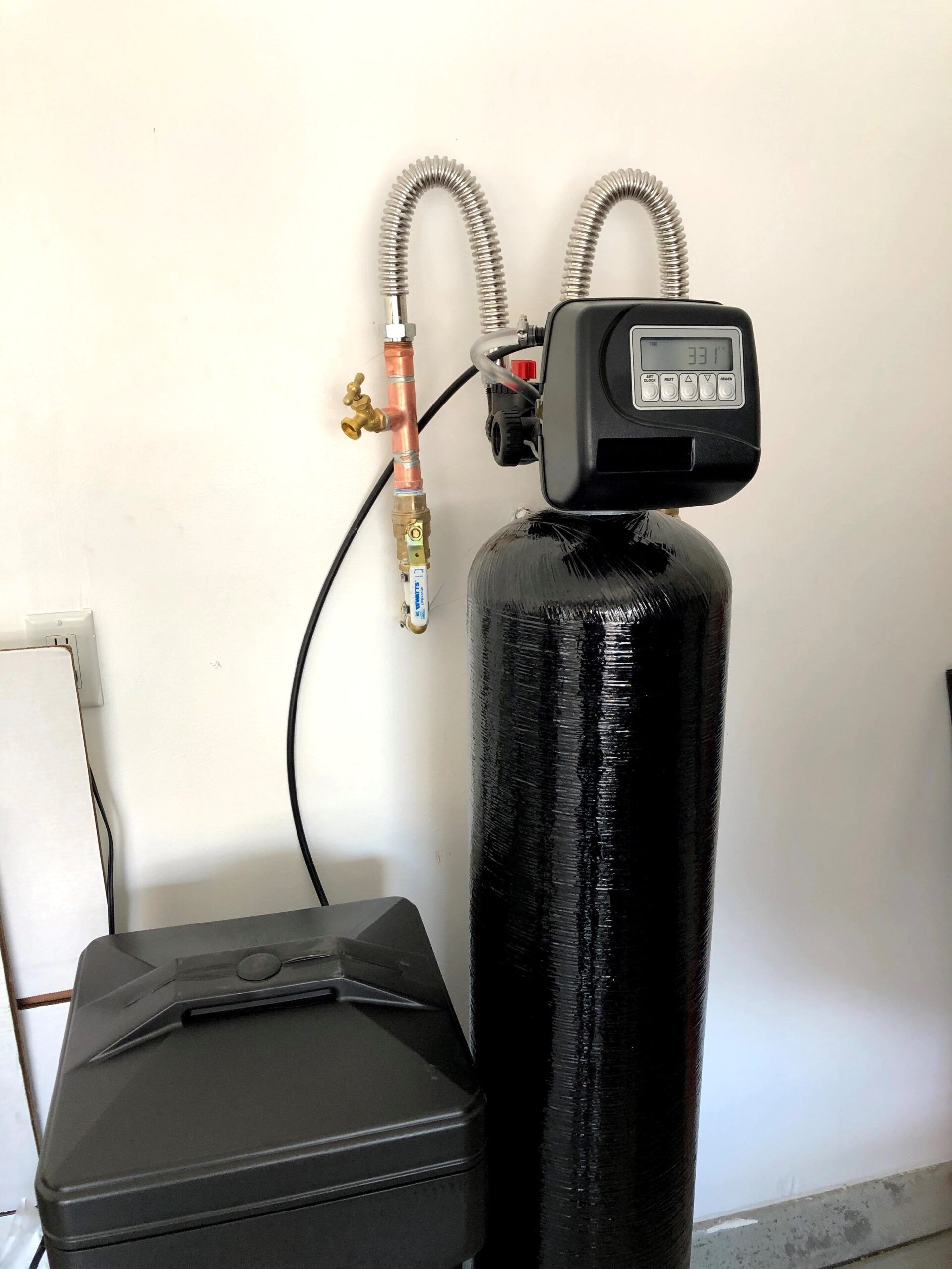 A black water filter is sitting next to a white wall.