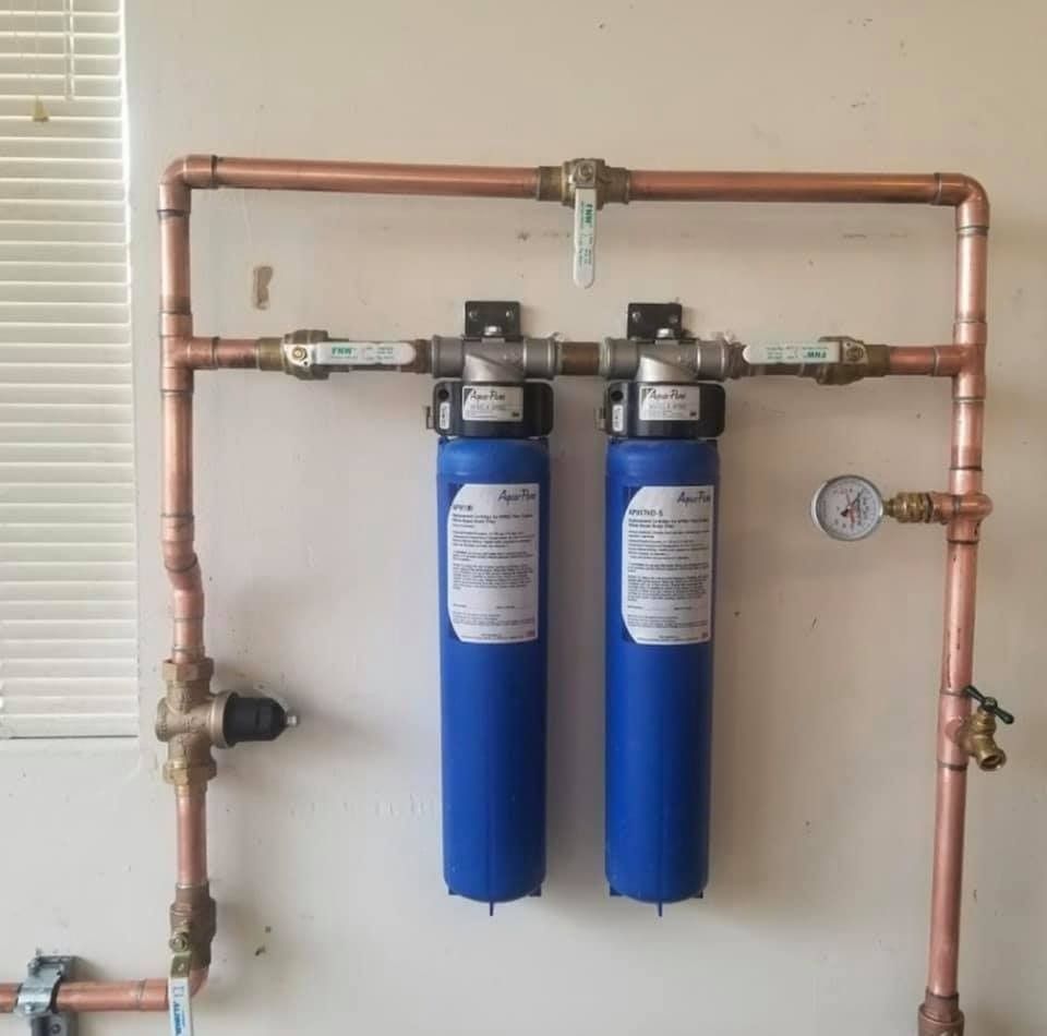 Two blue water filters are connected to copper pipes on a wall