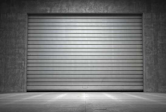 Una puerta de garaje está abierta en una habitación oscura con piso de concreto.