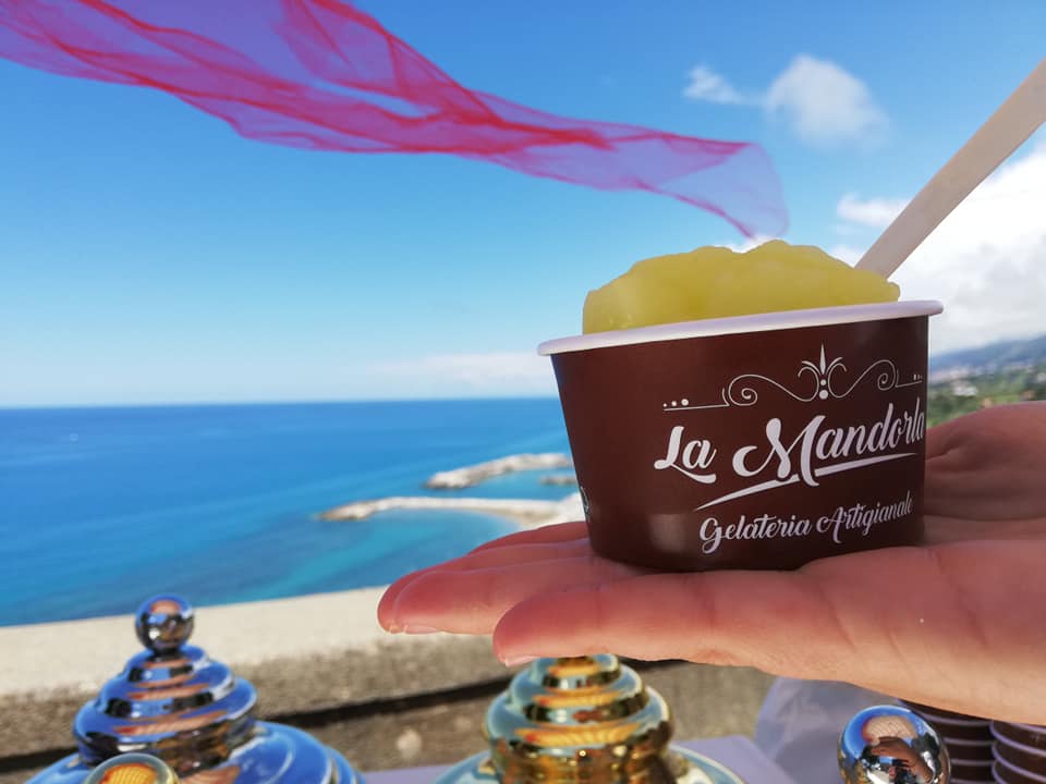 Una persona tiene in mano una coppa di gelato di fronte all'oceano