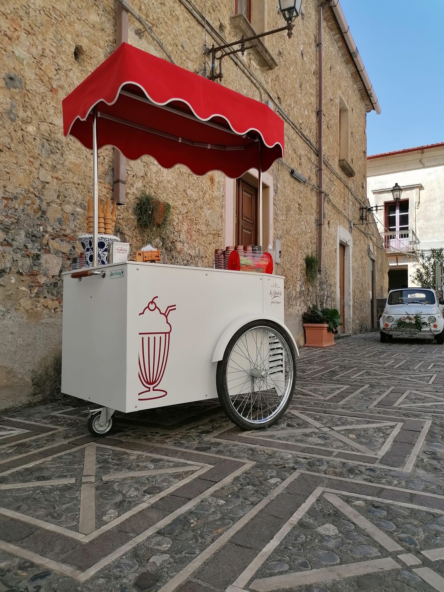 Un carretto bianco con una tenda rossa è parcheggiato davanti a un edificio in pietra.