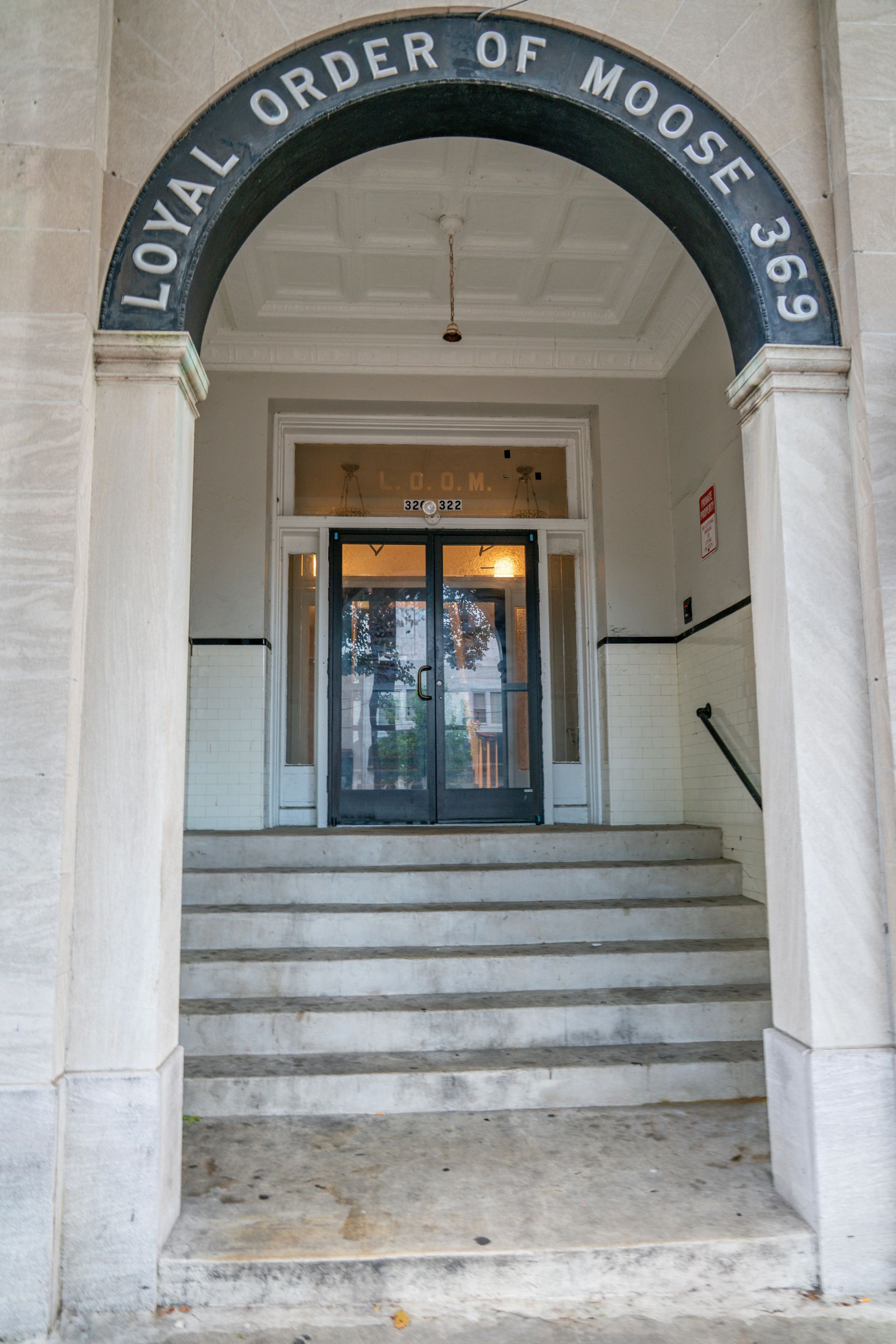 Photo of a building entrance with a small set of stairs leading up to the building entrance, set in and away from the street