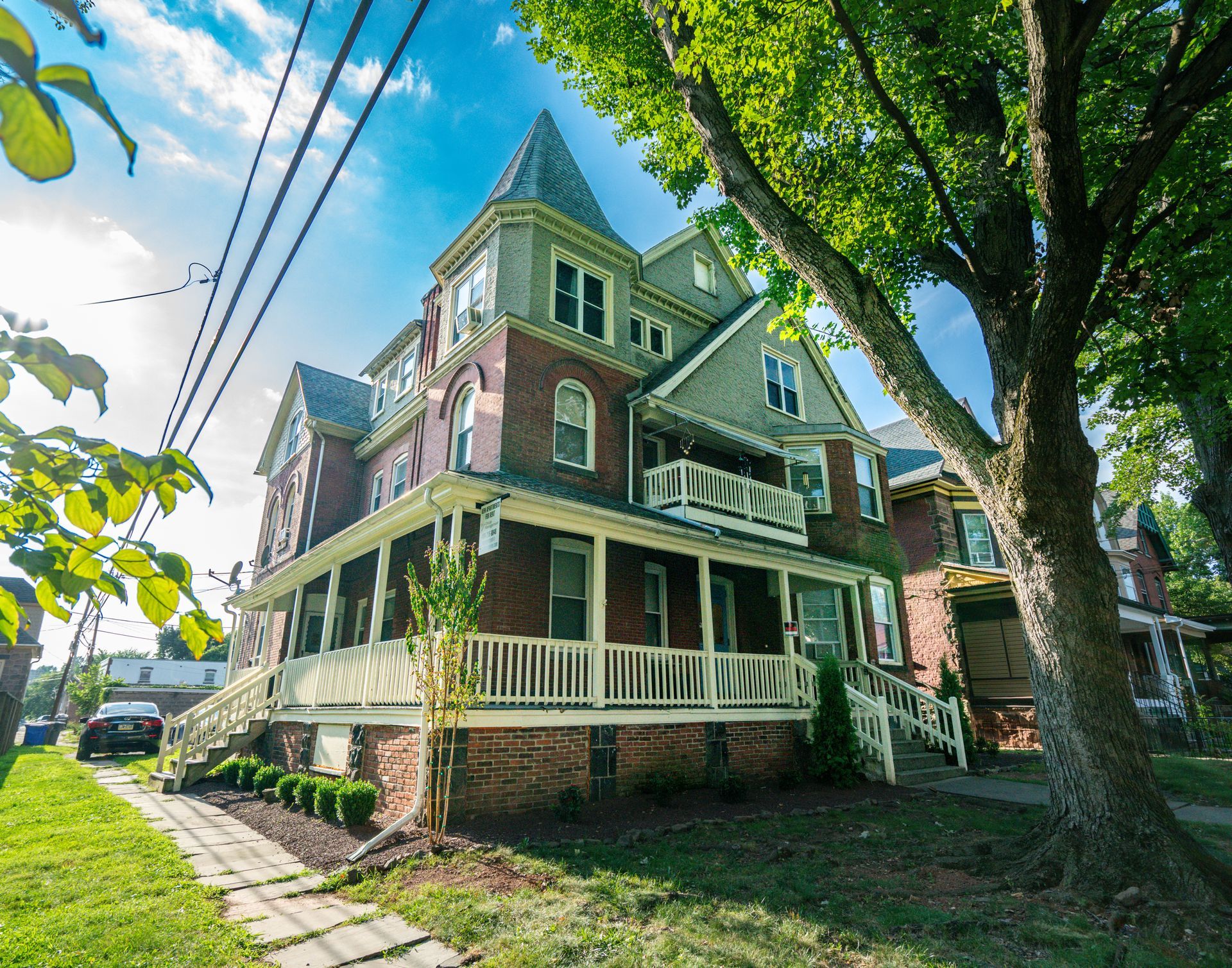 Photo of a 3 or 4 story building, with a wrap-around porch, seen from the lawn