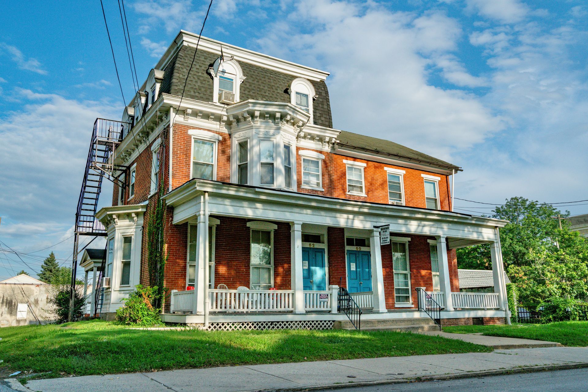 Photo of an 19th century or early 20th century home, 3 stories featuring red brick, combined with white and black elements, seen from the street