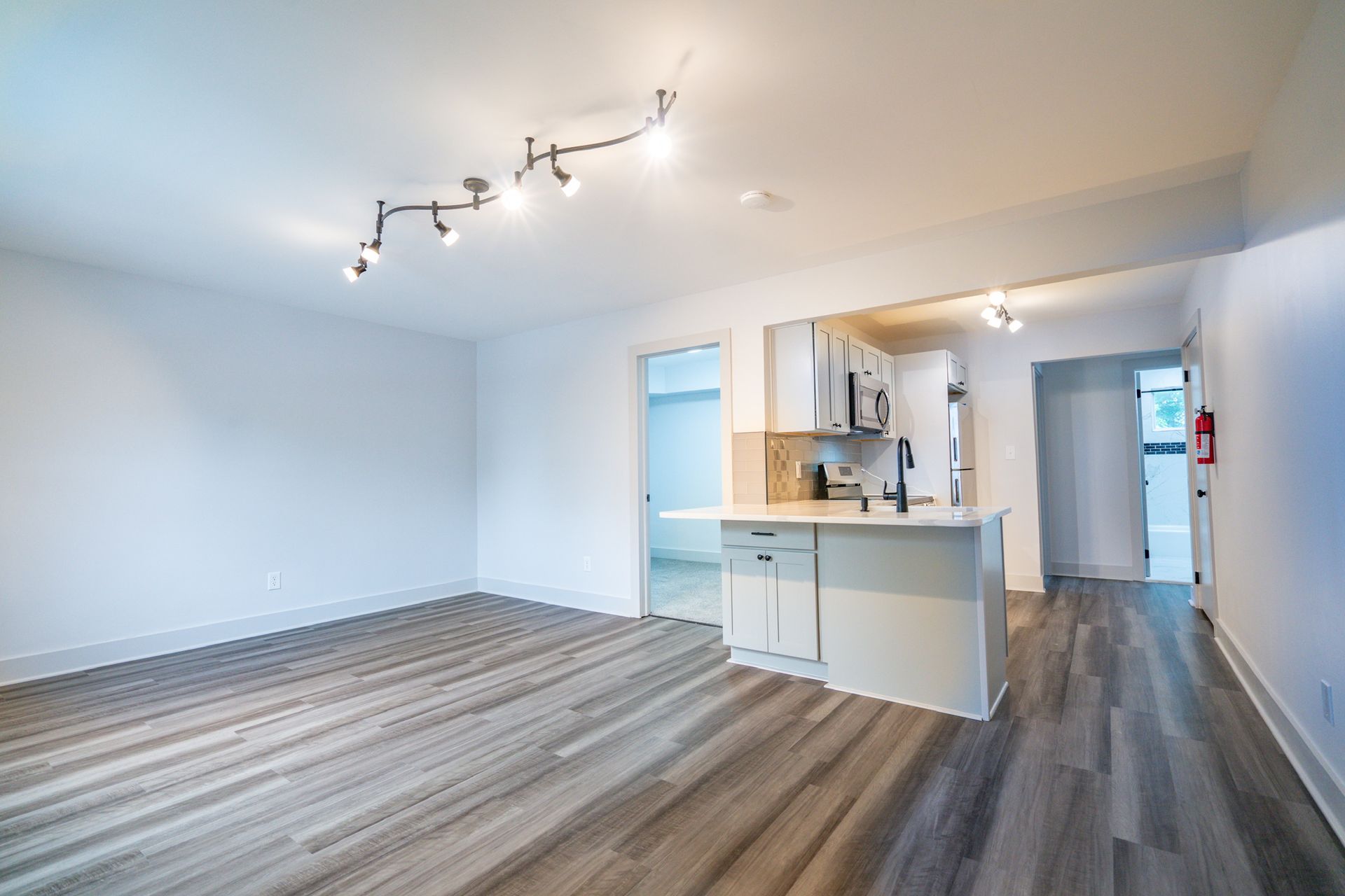 Photo of a white room with plenty of lighting and a kitchen in the background