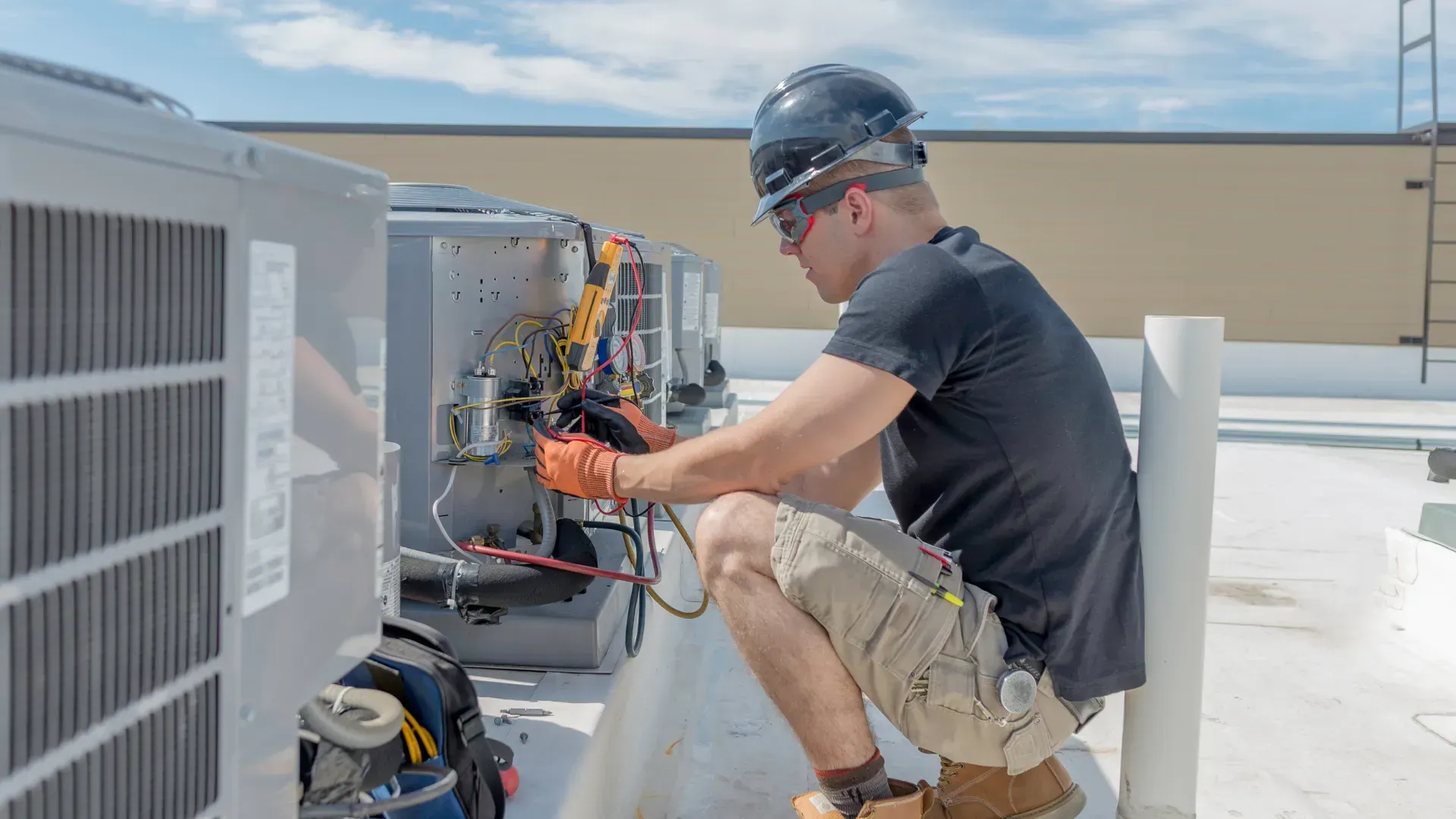 HVAC technician in a hard hat, testing an air conditioning unit on a rooftop, using a multimeter.