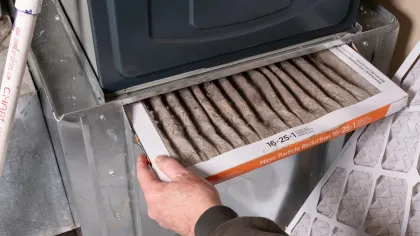 Person replacing a very dirty air filter in a furnace. The filter is gray with debris, and the furnace is metallic.