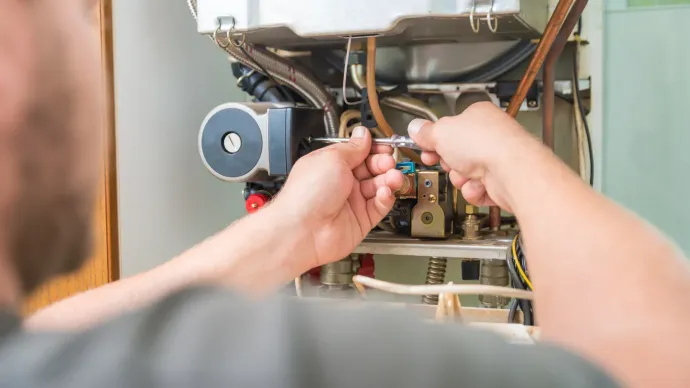 A person's hands working on a heating system with tools, indoors.