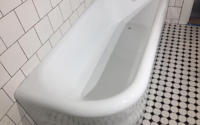 A white bathtub in a bathroom with white wall tiles and black and white patterned tile flooring.