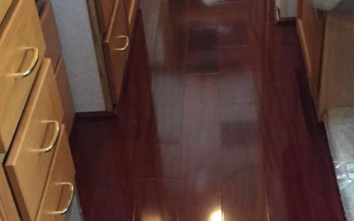 A narrow hallway with dark wood flooring, flanked by light-toned wooden cabinets with brass-colored handles.
